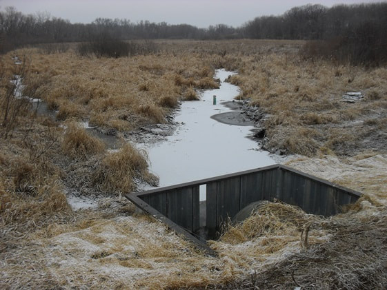Stream in wetland flowing into box weir. 